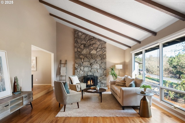 living room featuring vaulted ceiling with beams, a textured ceiling, a fireplace, and light wood-type flooring