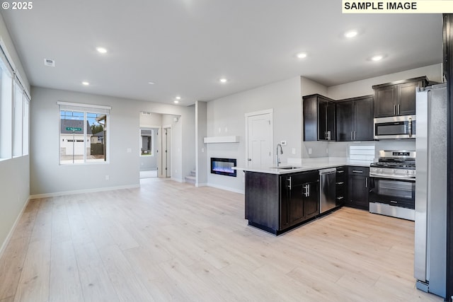 kitchen with stainless steel appliances, a peninsula, open floor plan, and light wood-style flooring