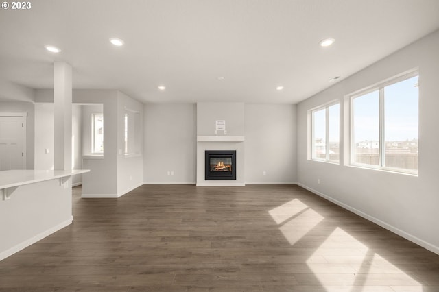 unfurnished living room with dark wood finished floors, a glass covered fireplace, recessed lighting, and baseboards