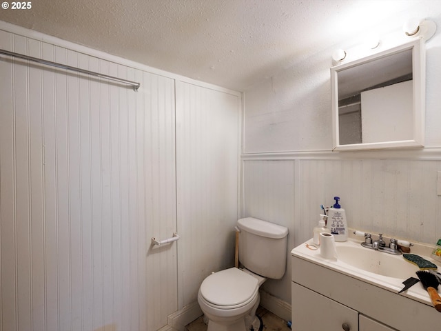 half bath with toilet, a wainscoted wall, a textured ceiling, and vanity