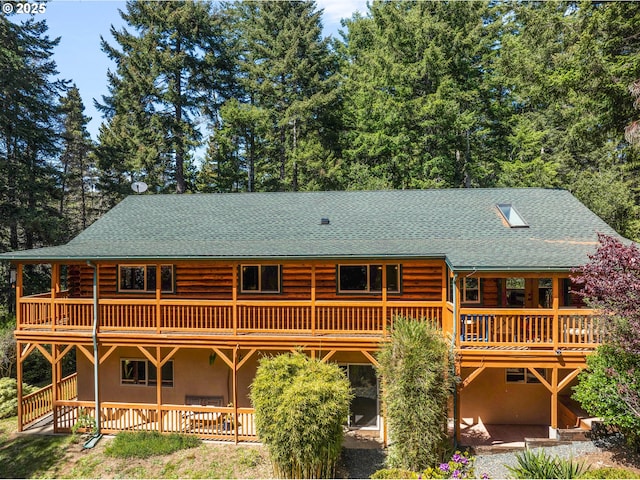 back of house featuring a shingled roof, log exterior, stucco siding, a deck, and a patio