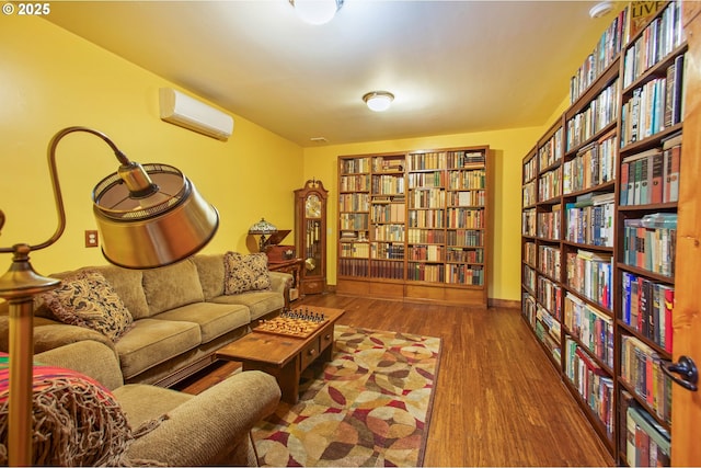 sitting room featuring wall of books, baseboards, wood finished floors, and an AC wall unit