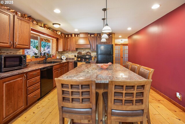 kitchen featuring a sink, light wood-style flooring, custom exhaust hood, and black appliances