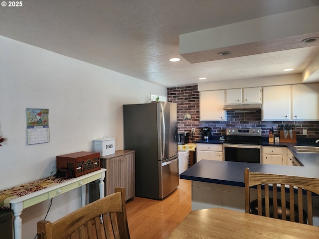 kitchen featuring stainless steel appliances, under cabinet range hood, light wood finished floors, white cabinetry, and dark countertops