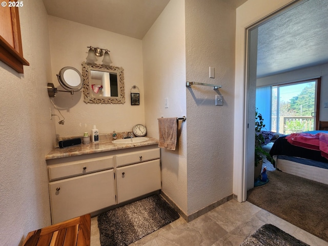 bathroom with baseboards, ensuite bathroom, vanity, and a textured wall