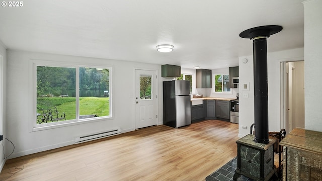 1298 N Tenmile, Lakeside, OR 97449 - kitchen featuring a wood stove, plenty of natural light, a baseboard heating unit, and appliances with stainless steel finishes