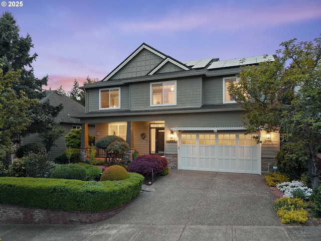 craftsman-style home with covered porch, driveway, solar panels, an attached garage, and stone siding
