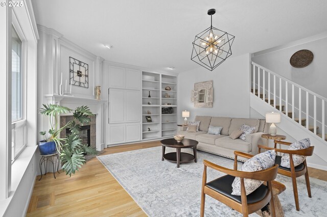 living room featuring an inviting chandelier, stairs, light wood-style floors, a high end fireplace, and built in shelves