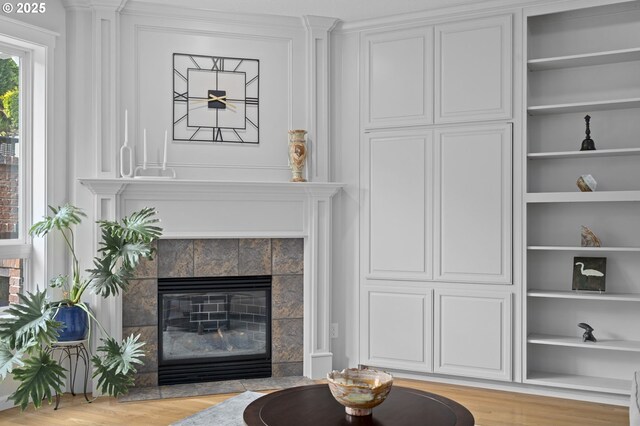 living area with built in features, light wood-style flooring, and a tile fireplace