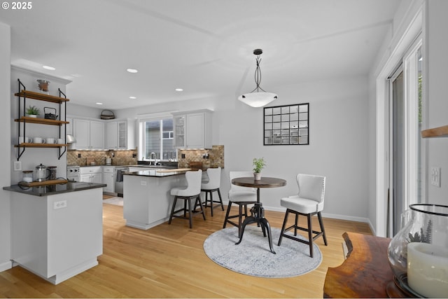 kitchen with backsplash, dark countertops, stainless steel dishwasher, open shelves, and a peninsula