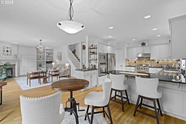 kitchen with a peninsula, a fireplace, dark countertops, a sink, and stainless steel appliances