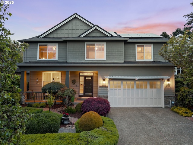 craftsman house with a porch, a garage, driveway, and solar panels