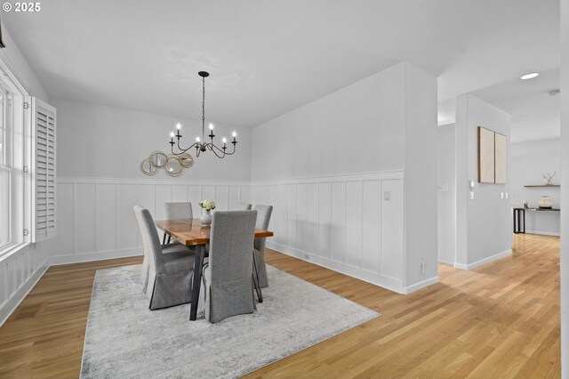 dining space featuring a wainscoted wall, light wood-type flooring, and a chandelier