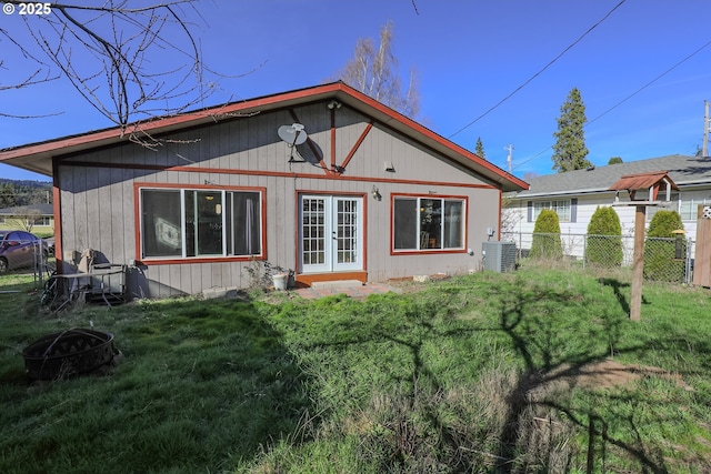 back of property with fence, an outdoor fire pit, central AC, french doors, and a yard