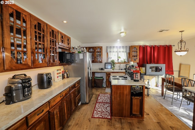 kitchen featuring glass insert cabinets, a center island, wood finished floors, and black microwave