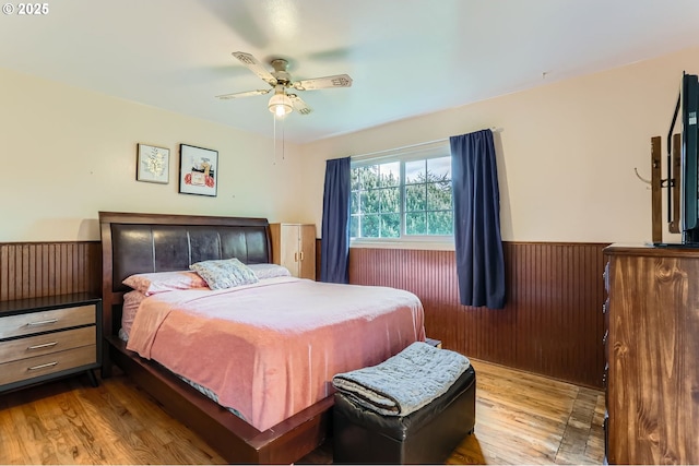bedroom with wood finished floors, wood walls, ceiling fan, and a wainscoted wall