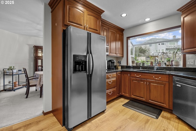 kitchen featuring sink, light hardwood / wood-style flooring, stainless steel fridge, black dishwasher, and dark stone counters