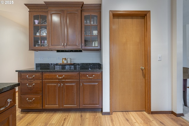 bar with dark stone countertops and light hardwood / wood-style floors