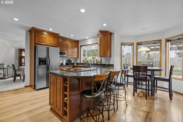 kitchen with decorative light fixtures, light wood-type flooring, dark stone countertops, appliances with stainless steel finishes, and a kitchen island