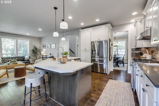 865 SW Trillium Ln, Portland, OR 97219 - kitchen with appliances with stainless steel finishes, under cabinet range hood, arched walkways, dark wood-style flooring, and a breakfast bar area