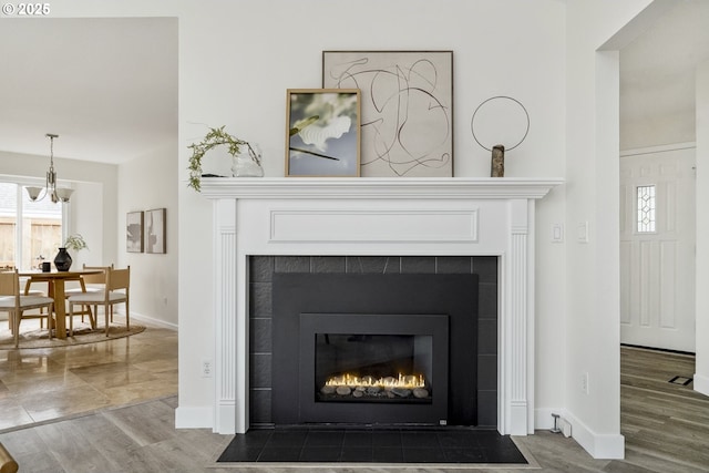 details featuring a tiled fireplace, a notable chandelier, wood finished floors, and baseboards