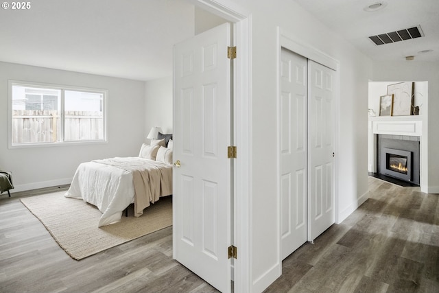 bedroom featuring visible vents, baseboards, a fireplace with flush hearth, wood finished floors, and a closet