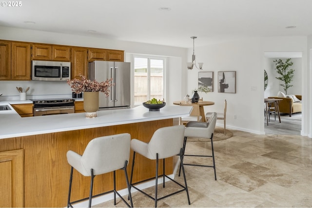 kitchen featuring a breakfast bar area, light countertops, brown cabinets, a peninsula, and stainless steel appliances