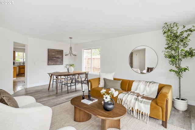 living area featuring baseboards, plenty of natural light, a chandelier, and light wood finished floors