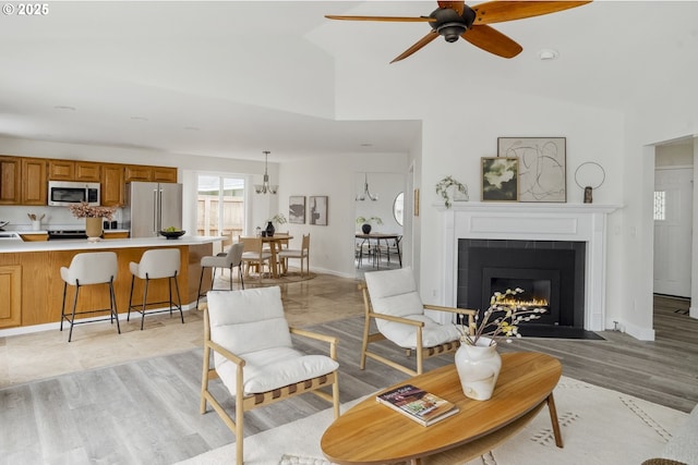 living room featuring baseboards, high vaulted ceiling, ceiling fan, and a tile fireplace