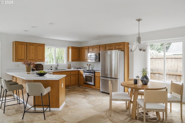 kitchen featuring a kitchen bar, appliances with stainless steel finishes, a peninsula, brown cabinetry, and light countertops