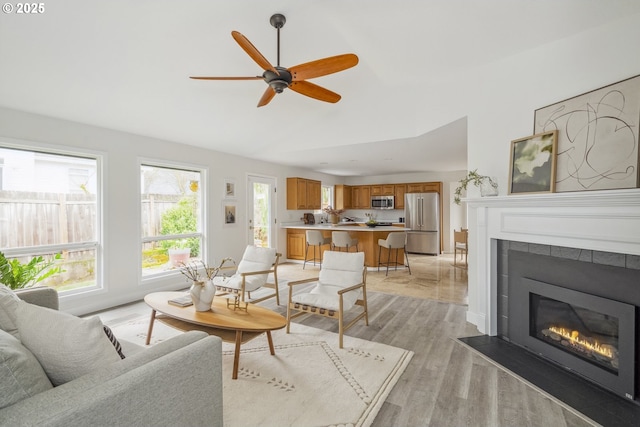 living area featuring light wood-type flooring, a ceiling fan, vaulted ceiling, and a tile fireplace