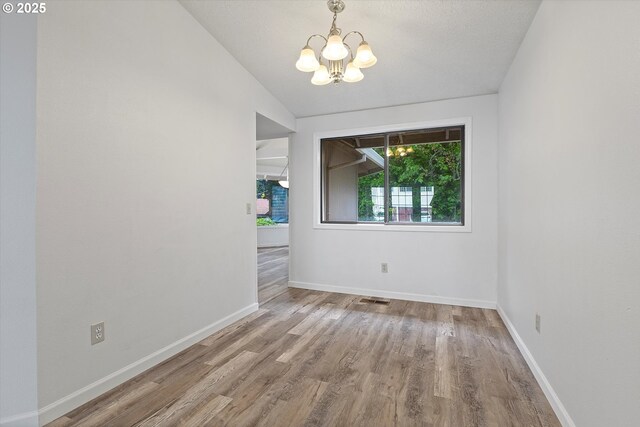 empty room with a chandelier, baseboards, wood finished floors, lofted ceiling, and visible vents