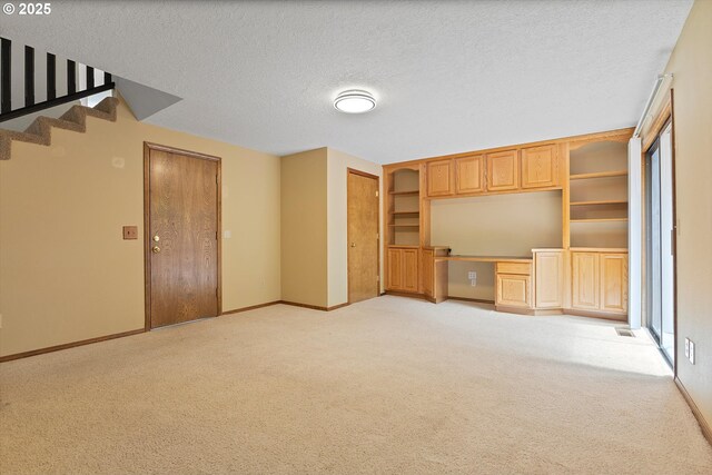 unfurnished living room featuring built in study area, baseboards, light carpet, and stairway