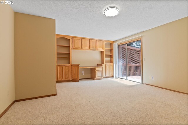 unfurnished living room featuring a textured ceiling, baseboards, light carpet, and built in study area