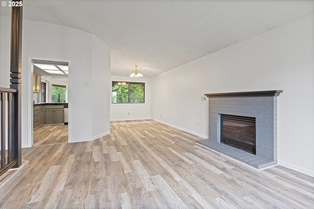 unfurnished living room featuring an inviting chandelier, a brick fireplace, light wood-style flooring, baseboards, and vaulted ceiling