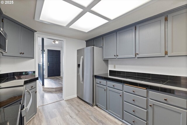 kitchen with appliances with stainless steel finishes, gray cabinets, light wood finished floors, and baseboards