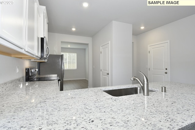 kitchen featuring white cabinetry, a sink, stainless steel appliances, light stone countertops, and wood finished floors
