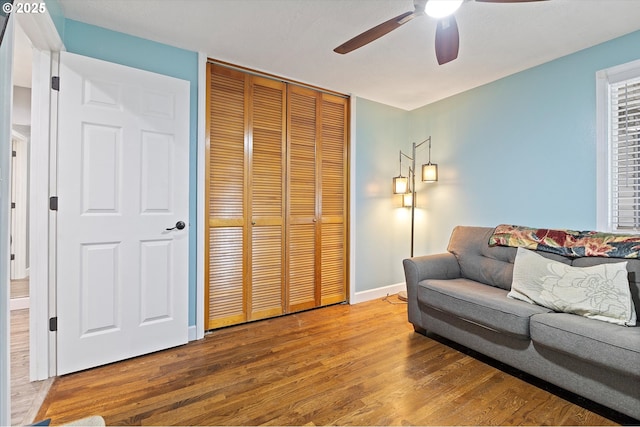 living area with baseboards, a ceiling fan, and wood finished floors