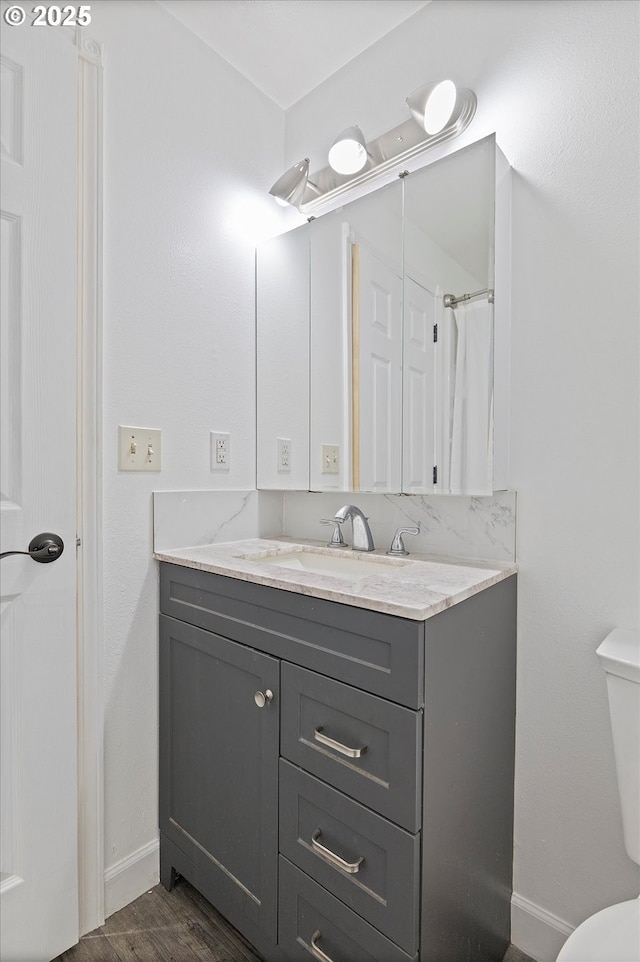 full bathroom featuring toilet, baseboards, wood finished floors, and vanity