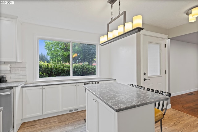 kitchen with a breakfast bar area, visible vents, stainless steel dishwasher, light wood-type flooring, and white cabinets