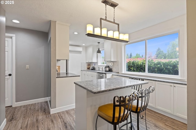 kitchen with light wood-style flooring, white cabinetry, a wall mounted AC, and dishwasher