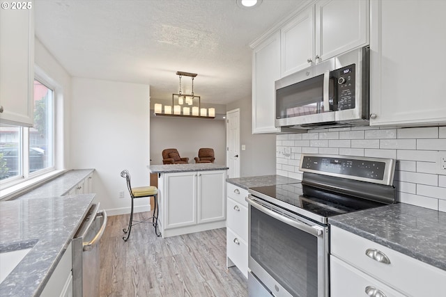 kitchen featuring light wood-style floors, a textured ceiling, stainless steel appliances, white cabinetry, and backsplash