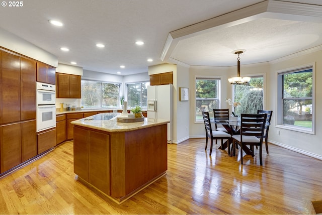 kitchen with hanging light fixtures, a kitchen island, white appliances, and light hardwood / wood-style floors