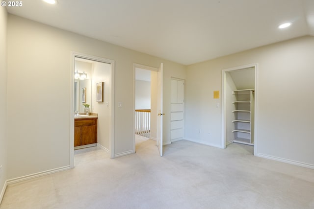 unfurnished bedroom with sink, a walk in closet, light colored carpet, ensuite bath, and a closet