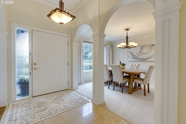 entrance foyer with an inviting chandelier, ornamental molding, light colored carpet, and decorative columns