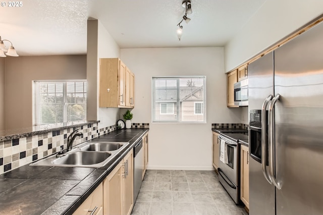 kitchen featuring dark countertops, appliances with stainless steel finishes, light brown cabinetry, and a sink