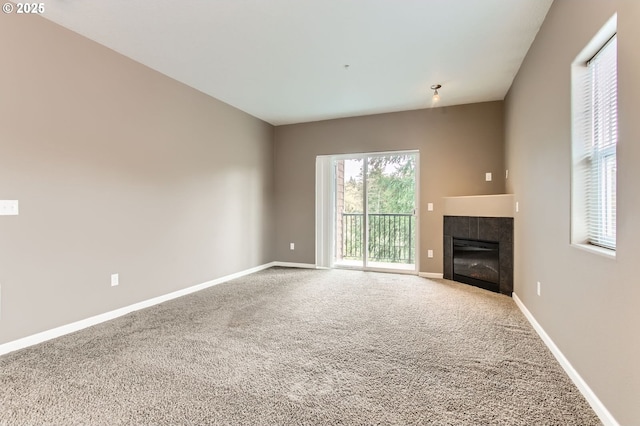 unfurnished living room with a tiled fireplace, baseboards, and carpet floors