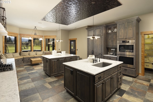 kitchen featuring a sink, dark brown cabinetry, a center island with sink, and double oven