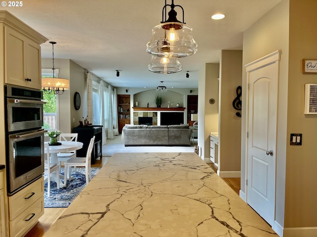 kitchen featuring double oven, light stone counters, hanging light fixtures, a chandelier, and baseboards