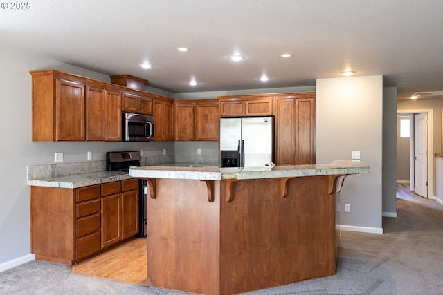 kitchen featuring appliances with stainless steel finishes, a kitchen bar, brown cabinetry, light countertops, and recessed lighting